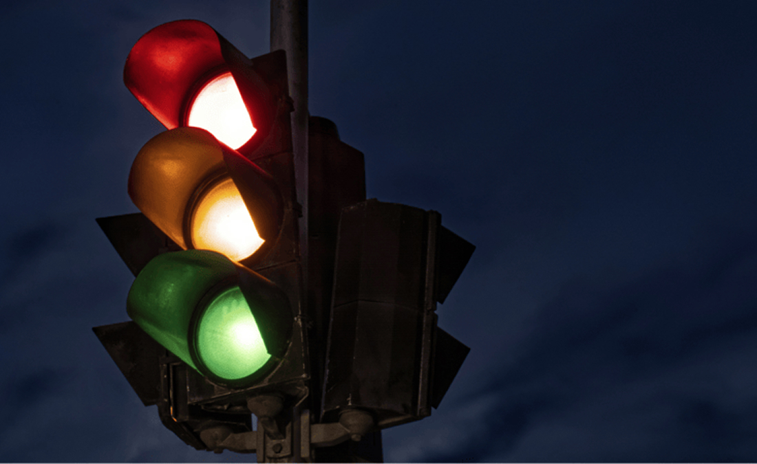A traffic light at night displaying red, yellow, and green signals simultaneously against a dark sky background.