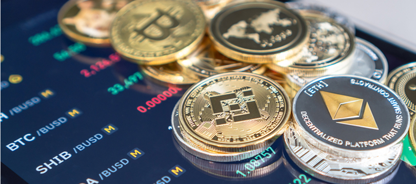 Stack of cryptocurrency coins including Bitcoin and Ethereum with a digital trading market screen in the background.