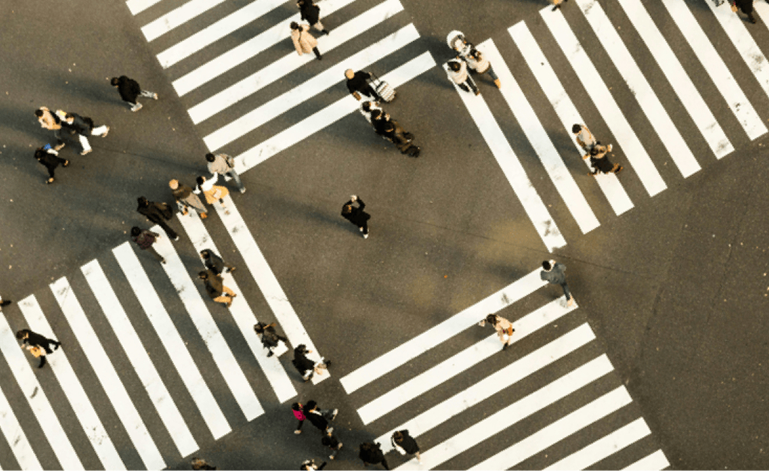 Aerial view of a busy city intersection with pedestrians walking across multiple striped crosswalks in different directions.