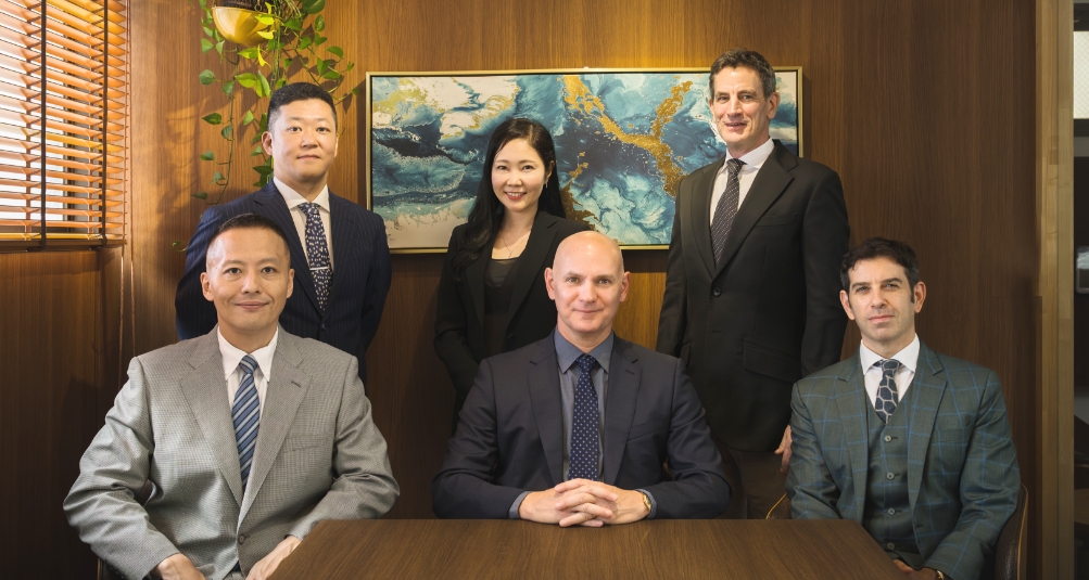 Group of business professionals in suits standing together and smiling, representing an executive search consulting team.