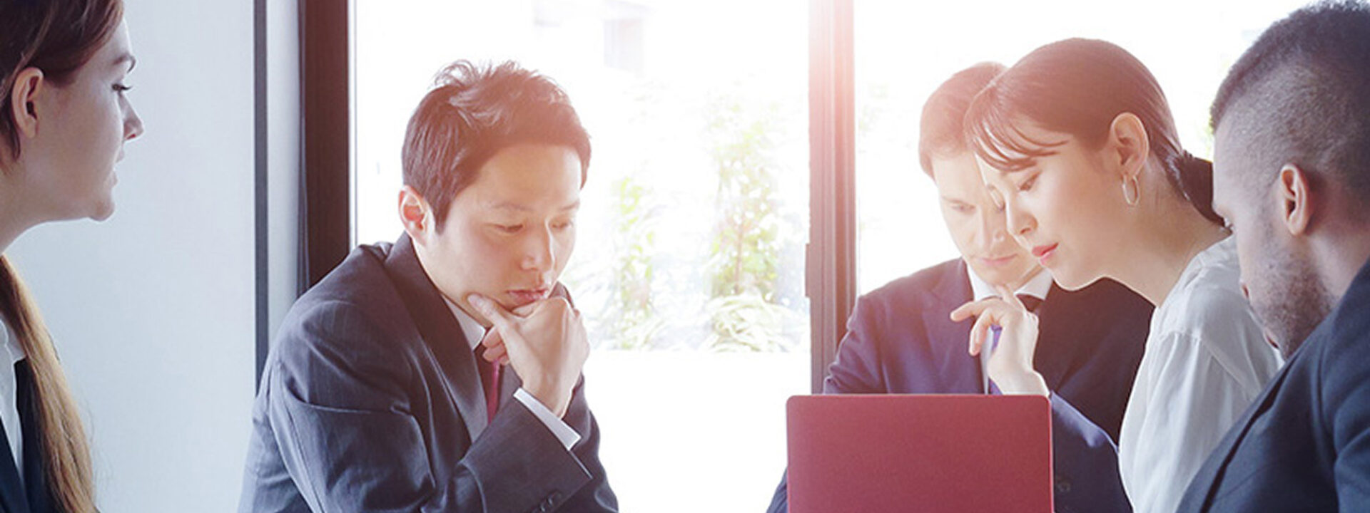 Professionals in a corporate setting reviewing documents and working together during a strategy meeting near a large window.