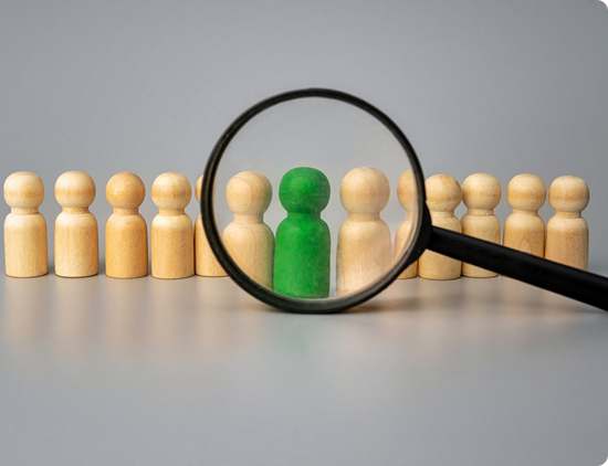 Illustration of a magnifying glass focusing on one figure among a group of wooden figurines.