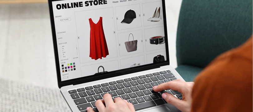 Person browsing an online fashion store on a laptop displaying a red dress, bags, and accessories.