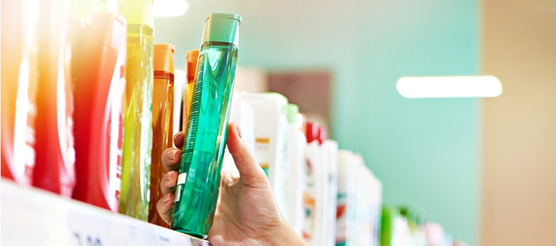 Consumer picking a green bottle from a store shelf with various FMCG products like shampoo and daily goods.