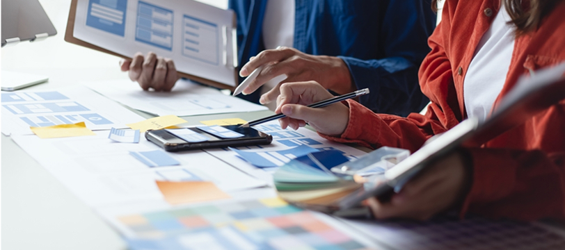 Marketing team discussing advertising and PR strategy with charts, documents, and color samples on the table.
