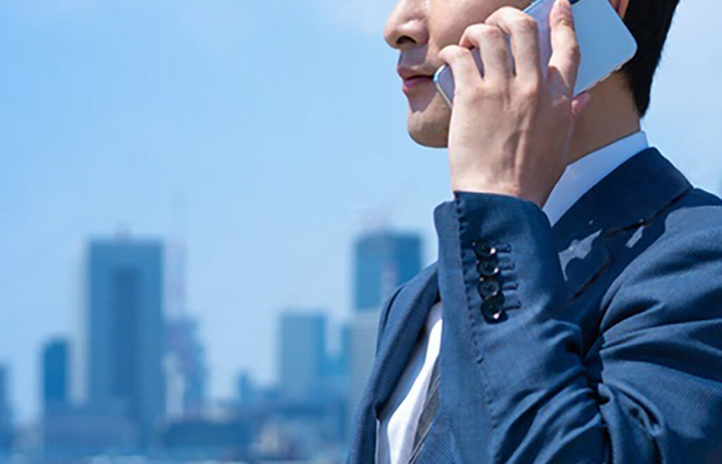 Business executive in a suit talking on a smartphone with city skyscrapers in the background.