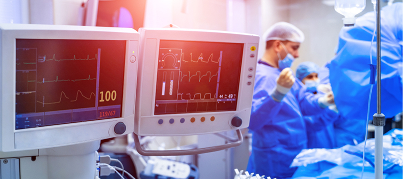 Doctors performing surgery in an operating room with medical monitors displaying vital signs in the foreground.
